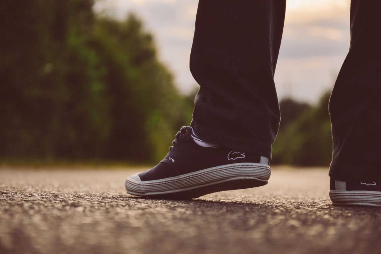 Close up of feet wearing sneakers walking down a paved tree lined road 