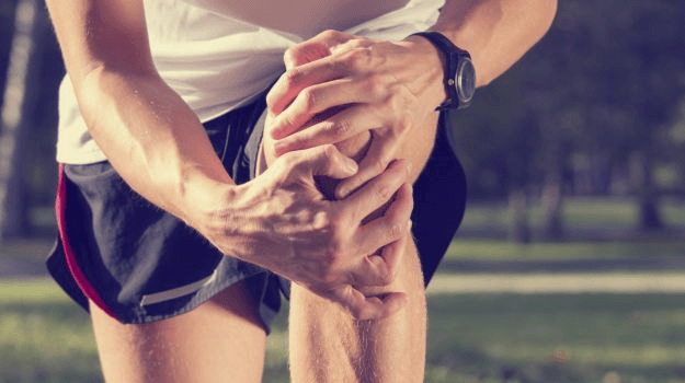 Close up of man in athletic gear grasping his knee in pain