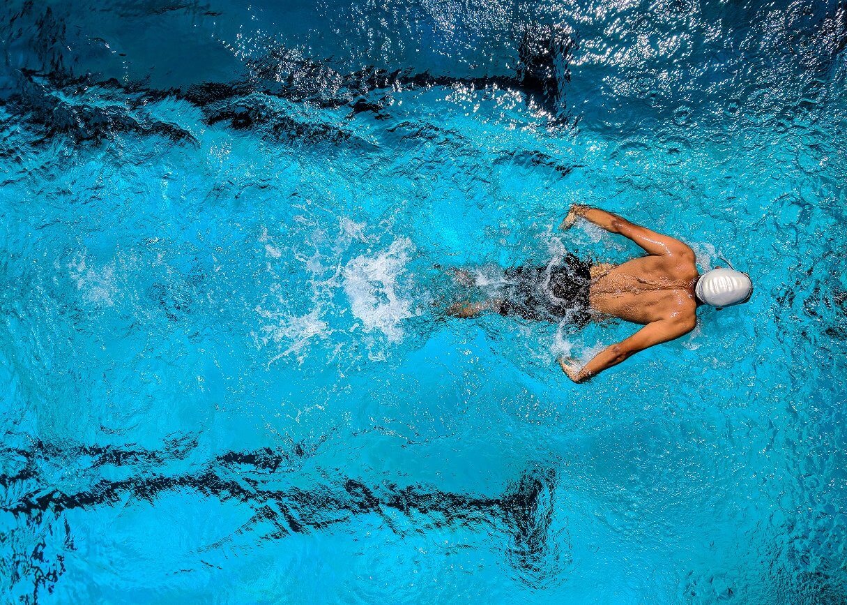 Man in white swim cap swimming laps in a pool