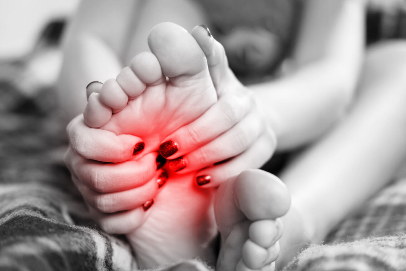 Black and white image of a person holding their foot which is glowing red to indicate pain caused by painful diabetic neuropathy