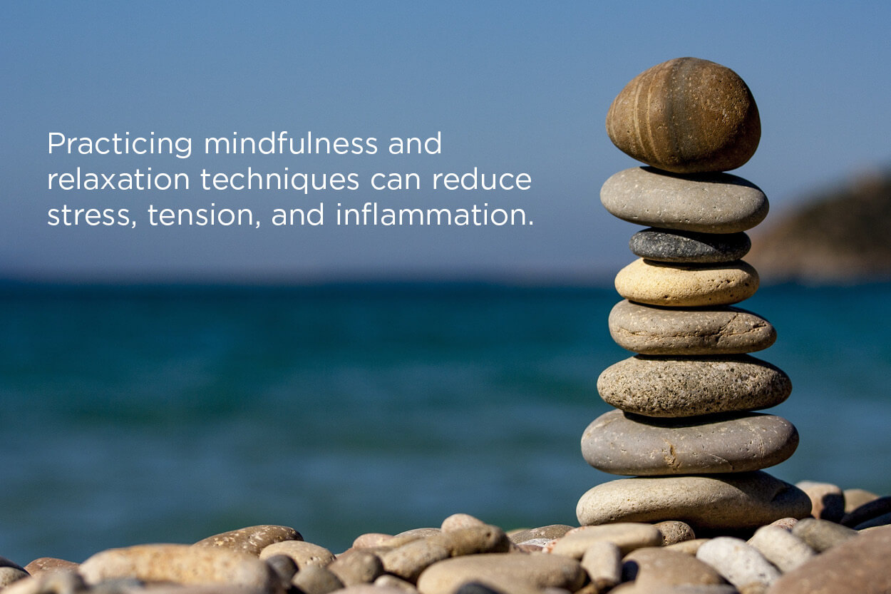Stack of stones on a beach overlooking the ocean with a fact about how mindfulness relieves stress.