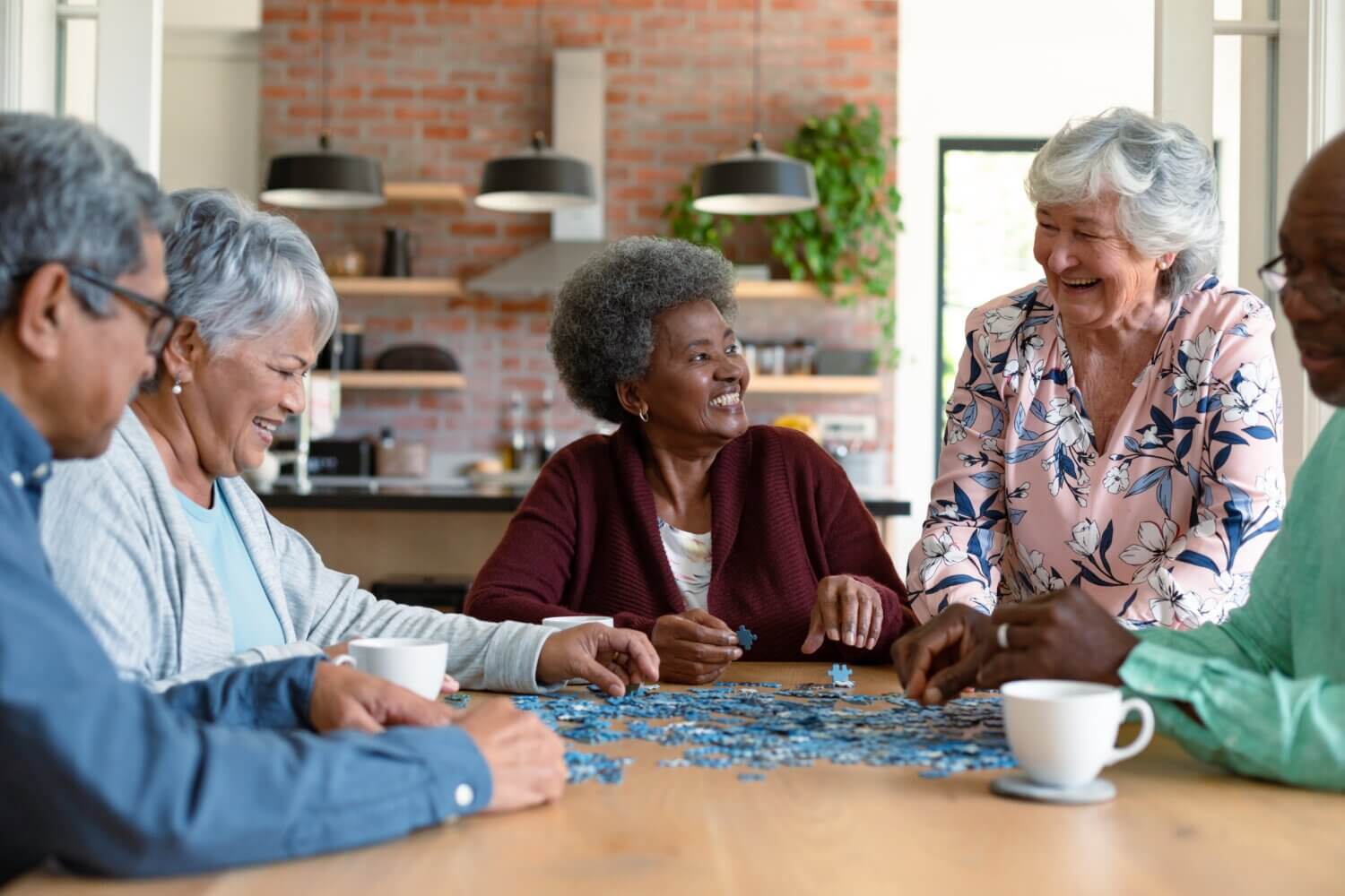 Group of diverse senior male and female friends doing puzzles and socializing at home