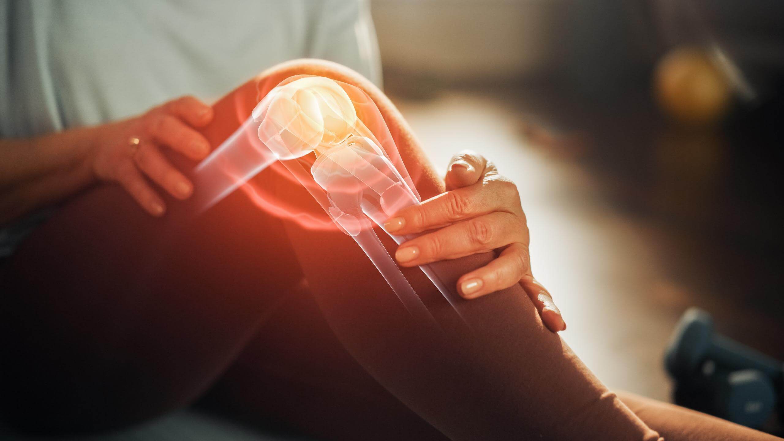 Close-up view of a middle-aged female holding her knee, which is displayed as an x-ray view and glowing red to indicate pain