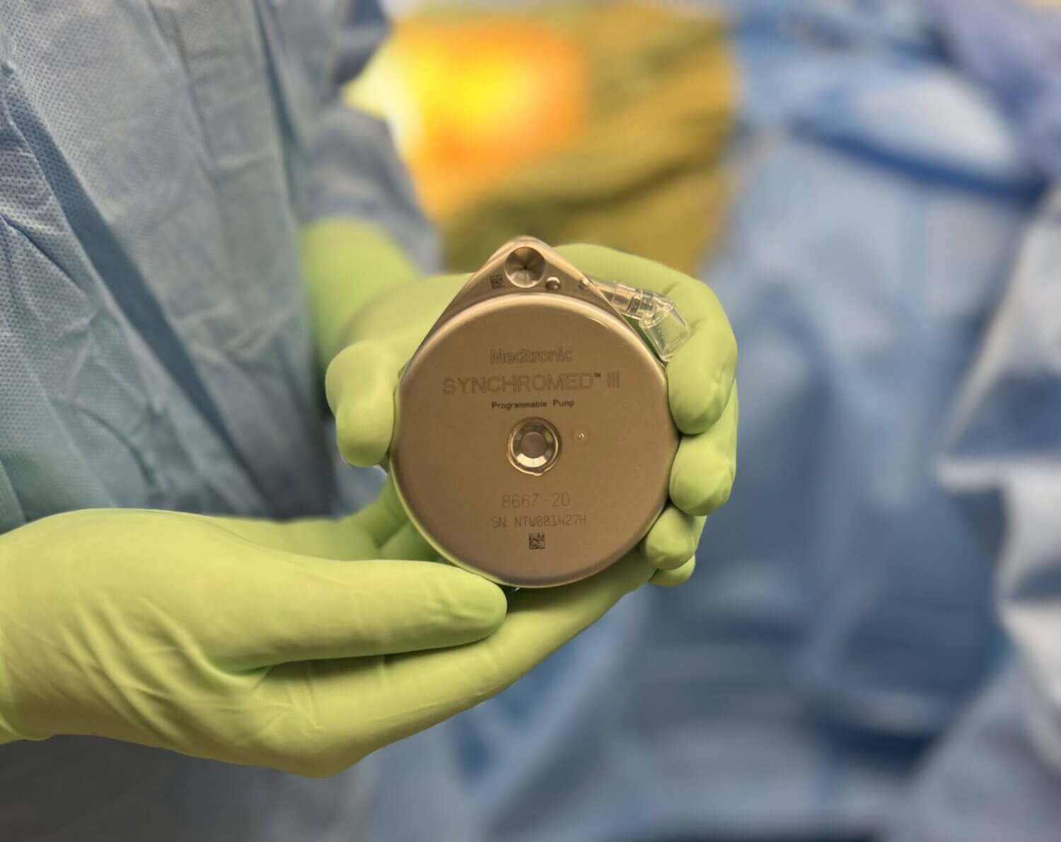 Close up image of two hands in surgical gloves holding the new SynchroMed™ III intrathecal pump system by Medtronic