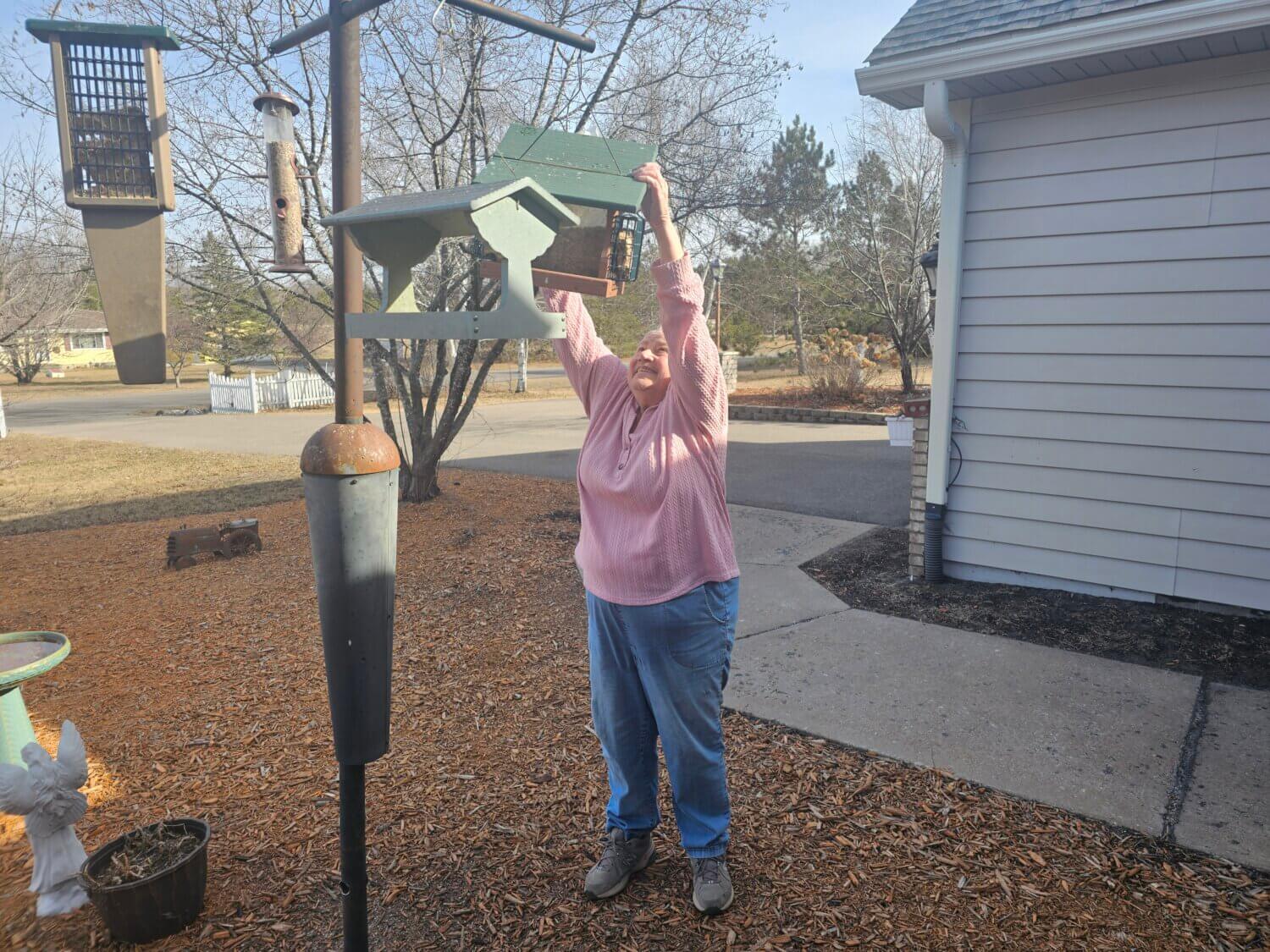Twin Cities Pain Clinic patient Cheri Haberle hanging a birdhouse in her yard.
