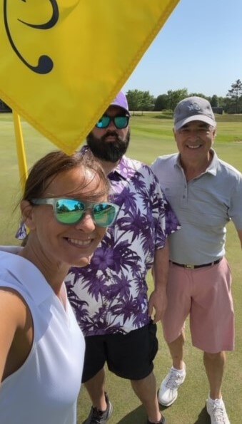 Two men and a woman next to a pin flag on a golf course