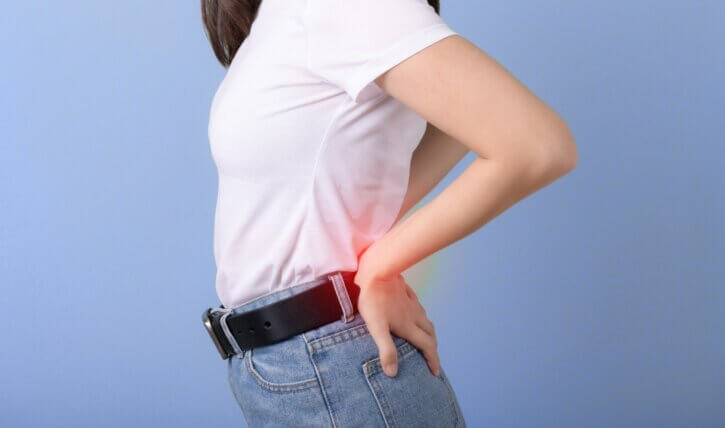 Shoulder to hip side view of young woman holding her lower back which is glowing red in pain