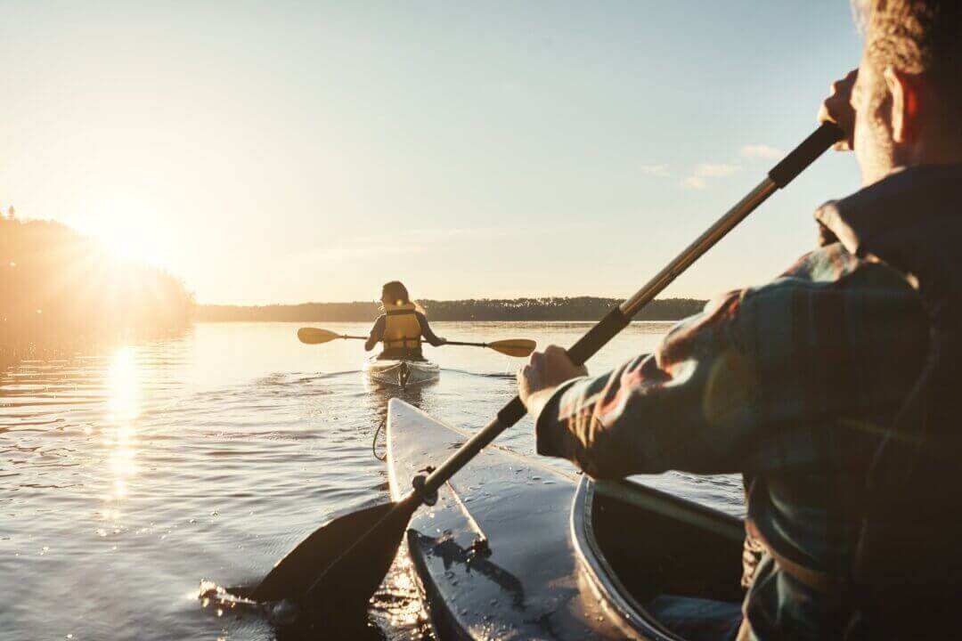 Young man and woman kayaking on a lake with shining sun peeking over trees