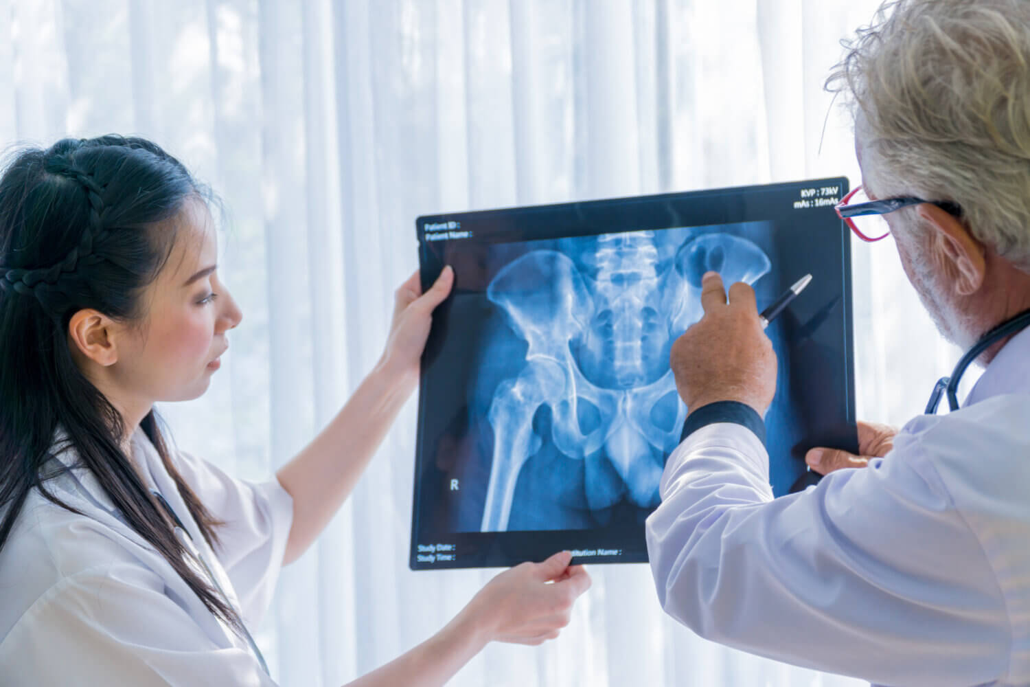 Senior doctor and young female nurse examining at the x-ray film of the human pelvis bones