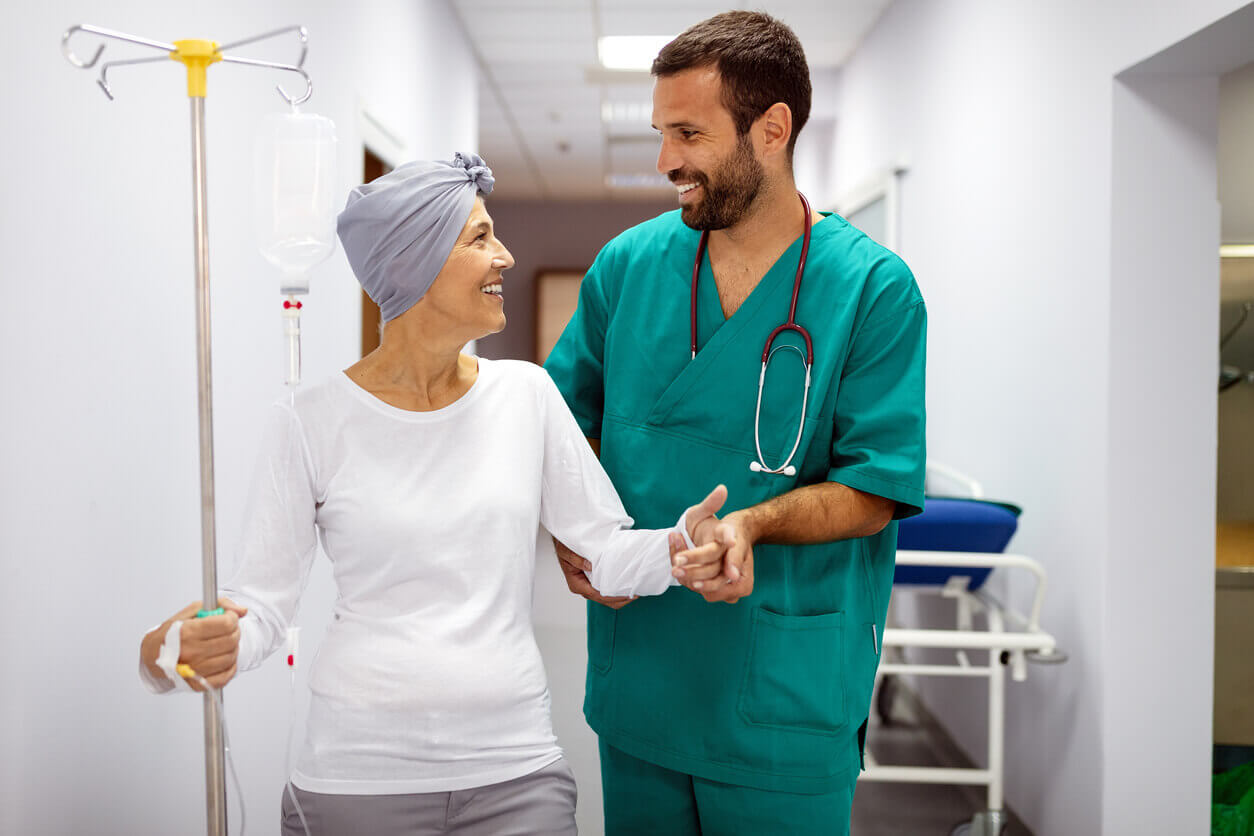Healthcare provider in green scrubs helping a cancer patient down a hospital hallway