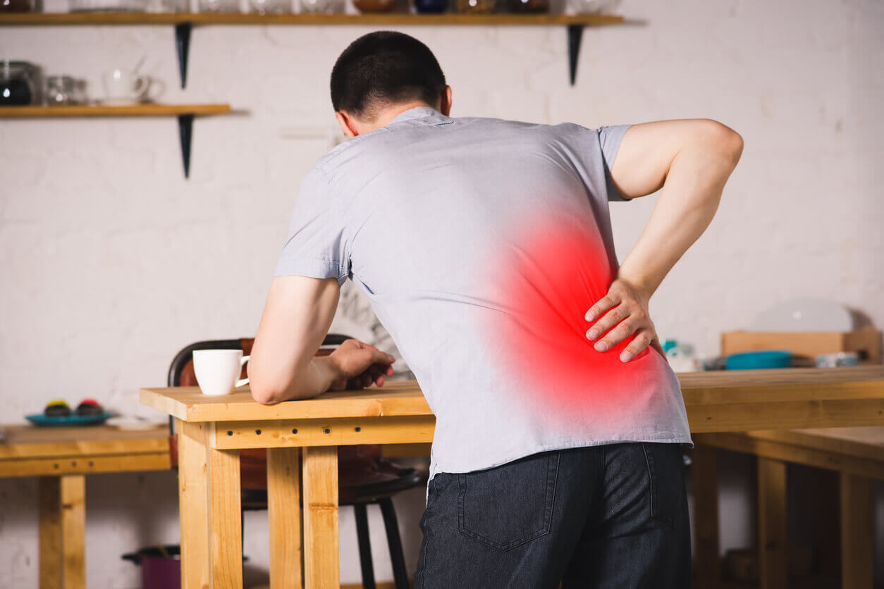 Male wearing t-shirt bending forward over a table while holding low back that is glowing red to indicate pain